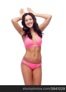 people, swimwear, summer beach and sexual concept - happy young woman in pink bikini swimsuit making bunny ears gesture