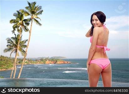 people, swimwear, summer, travel and sexual concept - happy young woman in pink bikini swimsuit looking back over Sri Lanka beach with palms swimming pool background