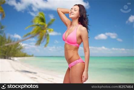 people, swimwear, tourism, travel and summer concept concept - happy young woman posing in pink bikini swimsuit over tropical beach background