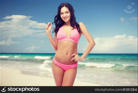 people, swimwear, tourism, travel and summer concept - happy sexy young woman posing in pink bikini swimsuit over beach background