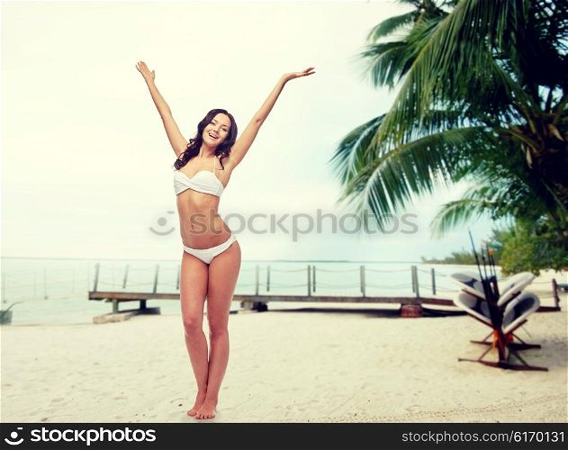 people, swimwear, tourism, travel and summer concept - happy young woman posing in white bikini swimsuit dancing with raised hands over berth on tropical beach background