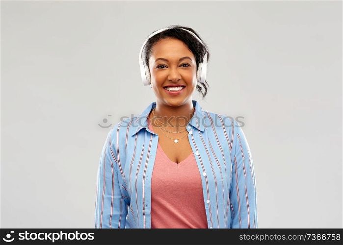 people, technology and audio equipment concept - happy african american young woman in headphones listening to music over pink background. african woman in headphones listening to music