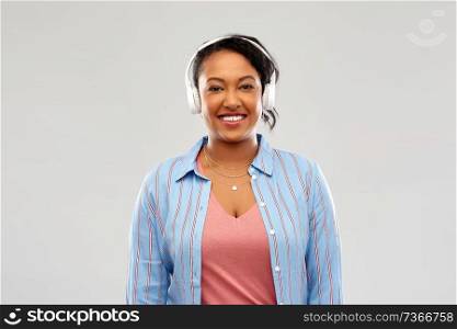 people, technology and audio equipment concept - happy african american young woman in headphones listening to music over pink background. african woman in headphones listening to music