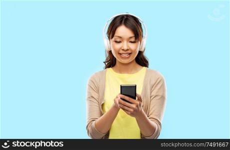 people, technology and audio equipment concept - happy asian young woman in headphones listening to music on smartphone over blue background. asian woman in headphones listening to music