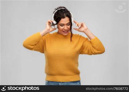 people, technology and audio equipment concept - happy smiling young woman with pierced nose in headphones listening to music over grey background. happy woman in headphones listening to music