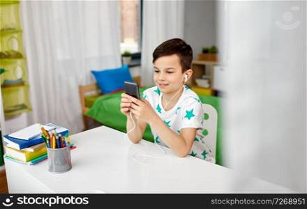 people, technology and childhood concept - happy smiling boy in earphones listening to music on smartphone at home. boy in earphones listening to music on smartphone