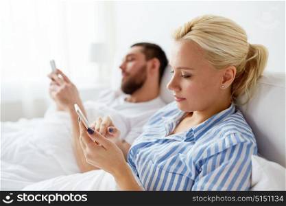 people, technology and communication concept - couple with smartphones in bed at home. couple with smartphones in bed at home