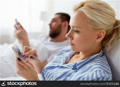 people, technology and communication concept - couple with smartphones in bed at home. couple with smartphones in bed at home