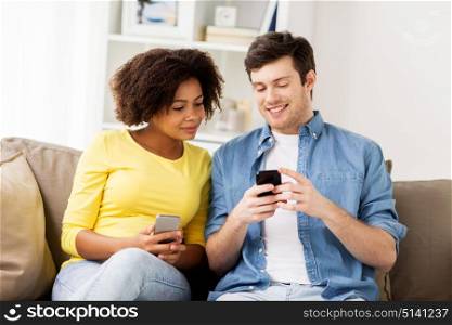 people, technology and communication concept - happy couple with smartphones networking or messaging at home. happy couple with smartphones at home