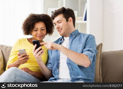 people, technology and communication concept - happy couple with smartphones networking or messaging at home. happy couple with smartphones at home