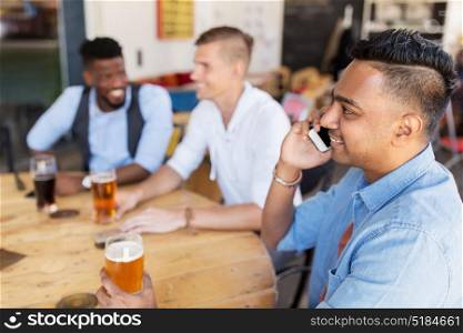 people, technology and communication concept - happy man calling on smartphone and drinking beer with friends at bar or pub. man calling on smartphone and drinking beer at bar