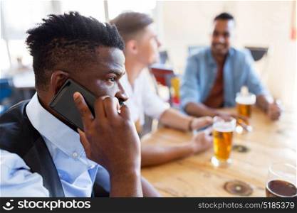 people, technology and communication concept - happy man calling on smartphone and drinking beer with friends at bar or pub. man calling on smartphone and drinking beer at bar