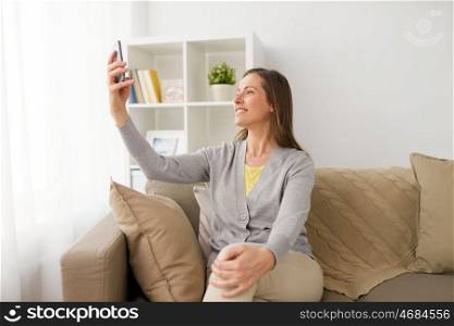 people, technology and communication concept - happy middle-aged woman taking selfie by smartphone at home. happy woman taking selfie by smartphone at home. happy woman taking selfie by smartphone at home