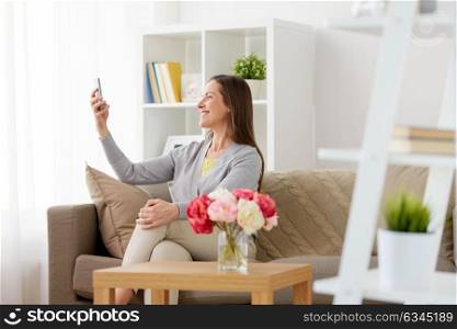 people, technology and communication concept - happy middle-aged woman taking selfie by smartphone at home. happy woman taking selfie by smartphone at home