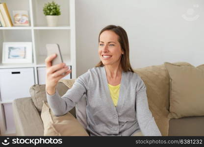 people, technology and communication concept - happy middle-aged woman taking selfie by smartphone at home. happy woman taking selfie by smartphone at home