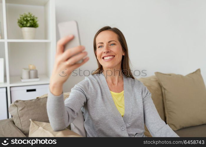 people, technology and communication concept - happy middle-aged woman taking selfie by smartphone at home. happy woman taking selfie by smartphone at home