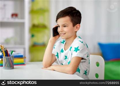 people, technology and communication concept - happy smiling boy calling on smartphone at home. happy boy calling on smartphone at home