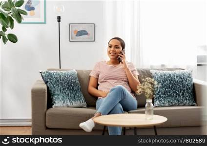 people, technology and communication concept - happy young african american woman calling on smartphone at home. african woman calling on smartphone at home