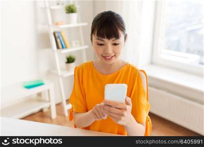 people, technology and communication concept - happy young asian woman texting message on smartphone at home. happy asian woman with smartphone at home