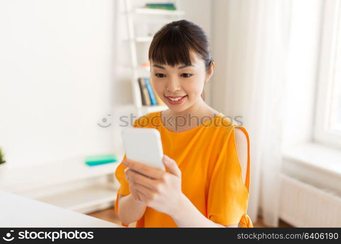 people, technology and communication concept - happy young asian woman texting message on smartphone at home. happy asian woman with smartphone at home