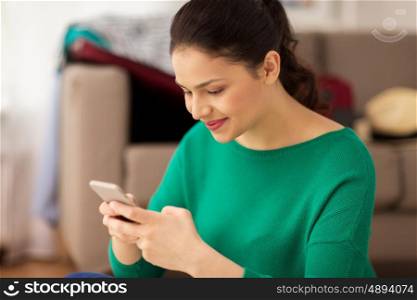 people, technology and communication concept - happy young woman sitting with smartphone at home