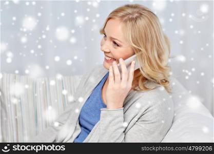 people, technology and communication concept - smiling woman calling on smartphone at home over snow
