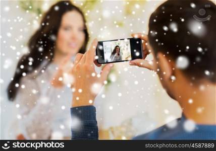 people, technology and dating concept - close up of man with smartphone taking picture of woman drinking tea at cafe or restaurant