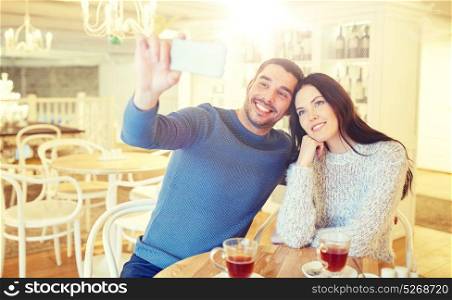 people, technology and dating concept - happy couple taking smartphone selfie and drinking tea at cafe or restaurant. couple taking smartphone selfie at cafe restaurant