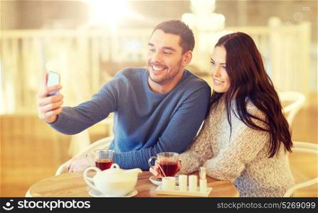 people, technology and dating concept - happy couple taking smartphone selfie and drinking tea at cafe or restaurant. couple taking smartphone selfie at cafe restaurant