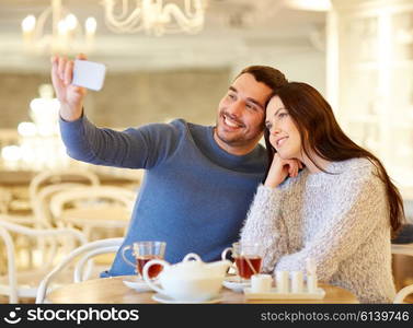 people, technology and dating concept - happy couple taking smartphone selfie and drinking tea at cafe or restaurant