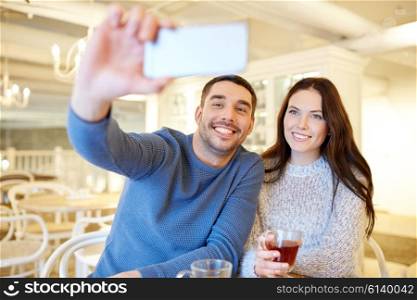 people, technology and dating concept - happy couple taking smartphone selfie and drinking tea at cafe or restaurant