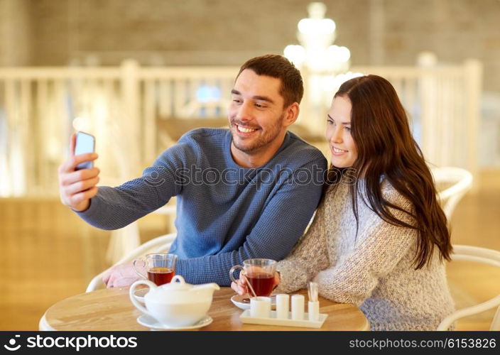 people, technology and dating concept - happy couple taking smartphone selfie and drinking tea at cafe or restaurant