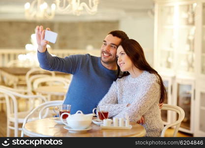 people, technology and dating concept - happy couple taking smartphone selfie and drinking tea at cafe or restaurant