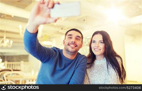 people, technology and dating concept - happy couple taking smartphone selfie at cafe or restaurant. couple taking smartphone selfie at cafe restaurant