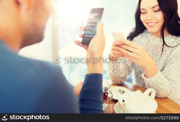 people, technology and dating concept - happy couple with smartphones drinking tea at cafe or restaurant. happy couple with smartphones drinking tea at cafe