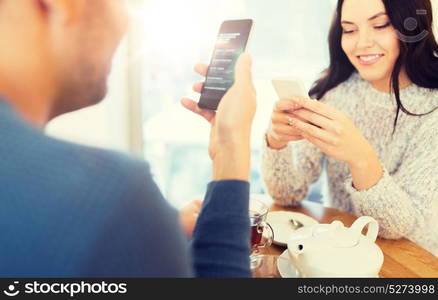 people, technology and dating concept - happy couple with smartphones drinking tea at cafe or restaurant. happy couple with smartphones drinking tea at cafe