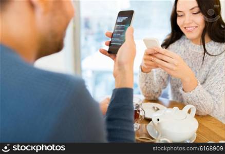 people, technology and dating concept - happy couple with smartphones drinking tea at cafe or restaurant