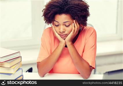 people, technology and education concept - bored african american young woman sitting at table with books and thinking at home