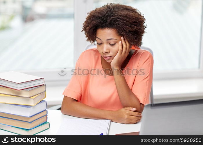people, technology and education concept - bored african american young woman sitting at table with laptop computer, books and notepad at home