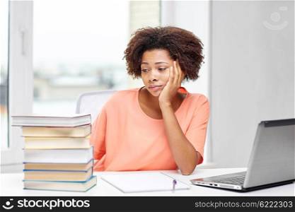 people, technology and education concept - bored african american young woman sitting at table with laptop computer, books and notepad at home