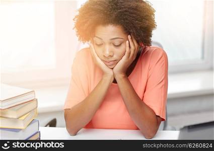 people, technology and education concept - bored african american young woman sitting at table with books and thinking at home