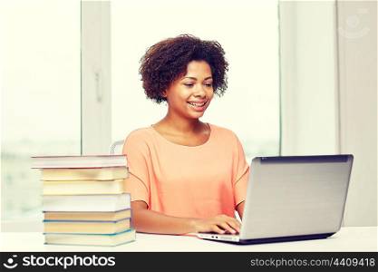 people, technology and education concept - happy african american young woman sitting at table with laptop computer and books at home