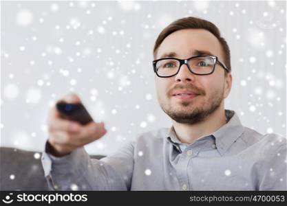 people, technology and entertainment concept - smiling man in eyeglasses with tv remote control at home over snow