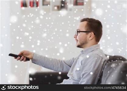 people, technology and entertainment concept - smiling man in eyeglasses with tv remote control at home over snow