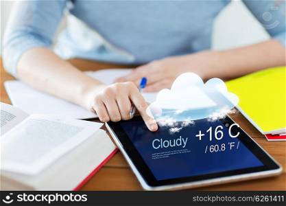 people, technology and forecast concept - close up of student woman with weather cast on tablet pc computer and notebook at home