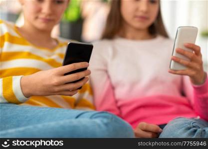 people, technology and friendship concept - close up of teenage girls with smartphones sitting on sofa at home. girls with smartphones sitting on sofa at home