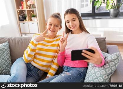 people, technology and friendship concept - happy teenage girls taking selfie with smartphone sitting on sofa at home. happy girls taking selfie with smartphone at home