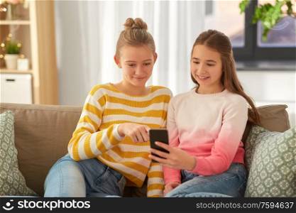 people, technology and friendship concept - happy teenage girls with smartphone sitting on sofa at home. happy teenage girls with smartphone at home