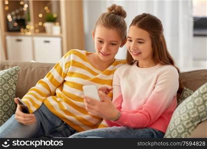 people, technology and friendship concept - happy teenage girls with smartphones sitting on sofa at home. happy teenage girls with smartphones at home