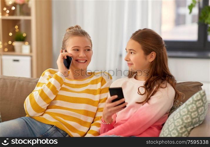 people, technology and friendship concept - happy teenage girls with smartphones sitting on sofa at home. happy teenage girls with smartphones at home